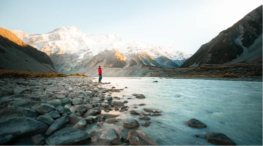 A person standing next to a river with mountains in the background in New Zealand.